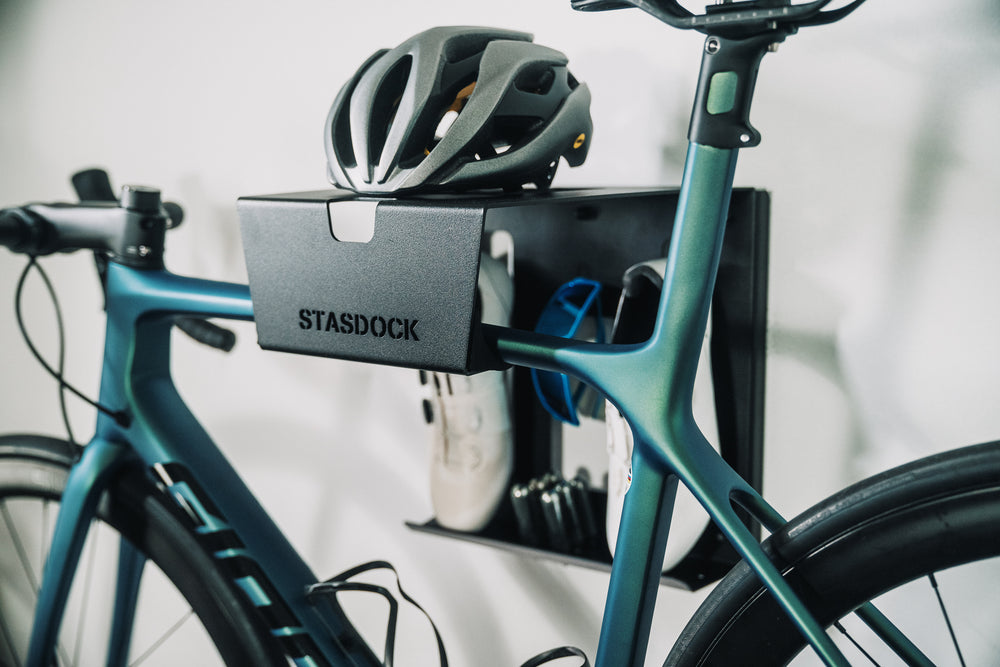 blue-green bike on black Stasdock wall mount. White shoes, blue glasses and grey helmet.